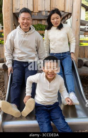Glückliche asiatische Familie, die Spaß auf einer Rutsche auf dem Spielplatz hat Stockfoto