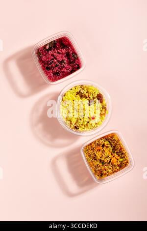 Vorgefertigte Quinoa- und Bulgur-Salate mit Gemüse und Sauce auf rosa Tisch. Schnelles Essen für unterwegs oder in der Mittagspause, Zeit sparen, fertig zu essen Stockfoto