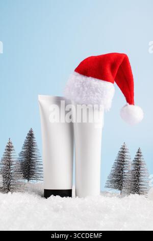 Schönheitskonzept für die Winterpflege mit Kosmetikprodukten mit Weihnachtsmütze, Weihnachtsdekorationen auf blauem Hintergrund, Vorderansicht, Kopierraum Stockfoto