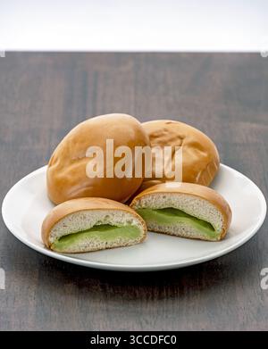 Weiche Brötchen gefüllt mit cremigem Pandan-Pudding sind auf weißem Teller angeordnet, um eine köstliche und einladende Präsentation zu kreieren. Glatte Textur Stockfoto