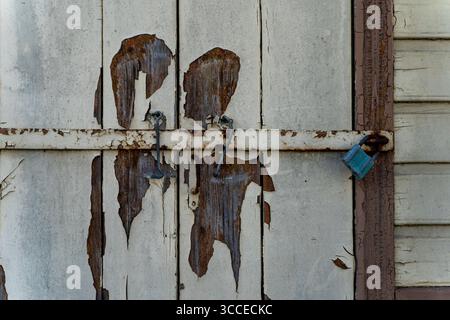 Nahaufnahme alter verwitterter Holzläden mit abblätternder Farbe und rostigem Schloss. Stockfoto
