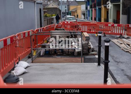 Urbane Straßenszene, die einen laufenden Gehsteig darstellt, umgeben von temporären Barrieren und Ausrüstungen unter einer strukturierten Anordnung Stockfoto