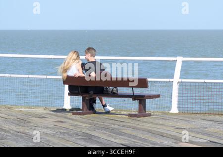 Ein junges Paar sitzt auf einer Bank und blickt auf das Meer am Ende des Piers UK Stockfoto
