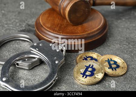 Kryptowährung. Bitcoins, Richtergabel und Handschellen auf grauem Tisch, Nahaufnahme Stockfoto