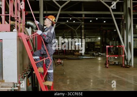 Frau, die Helm trägt, die industrielle Leiter in der Fabrik klettert Stockfoto