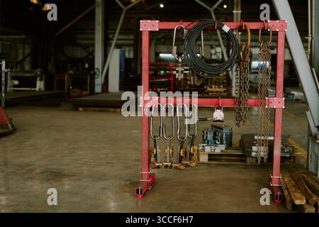 Industrielle Metallketten und Haken hängen am Roten Regal im Lagerbereich Stockfoto