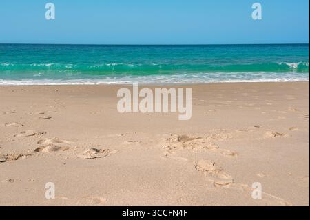 Sanfte türkisfarbene Meereswellen, die rhythmisch am Ufer eines unberührten Sandstrandes zusammenbrechen, schaffen ein ruhiges und einladendes Paradies zum Entspannen und Stockfoto