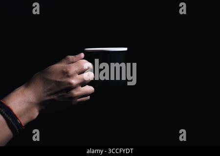 Hände halten eine Tasse schwarzen Kaffee auf schwarzem Hintergrund mit hohem Kontrast Stockfoto