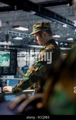 Soldat im Server-Hub, der Berichte auf der Workstation-Überwachung für Datenbetrieb überprüft. Informationsexperte der Armee trägt einheitliche Überwachungssysteme mit Display im operativen Rechenzentrum Stockfoto