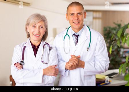 Zwei lächelnde, selbstbewusste Ärzte stehen in der Arztpraxis Stockfoto