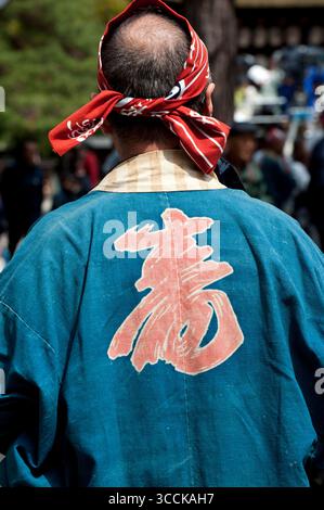 Ein japanischer Senior mit einem Haarband „Hachimaki“ (鉢巻) und einem Kurzmantel für das Festival „Happi“ (法被 oder 半被) mit dem Kanji-Charakter für Langlebigkeit (寿), Japan. Stockfoto