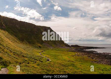 Eine Gruppe von Menschen läuft auf einem Weg in einem grasbewachsenen Feld. Der Himmel ist bewölkt und die Sonne scheint Stockfoto