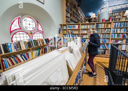 Eine junge Frau, die sich Vintage-Drucke und Karten in Leakey's Bookshop, Church Street, Inverness, Highland, Schottland anschaut. Vereinigtes Königreich Stockfoto