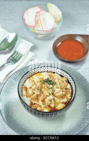Reisbrei serviert mit geriebenem Chähnchen, Cakwe, Crackern und Chili Stockfoto