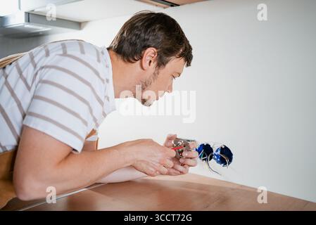 Qualifizierter Elektriker, der bei der Renovierung der Küche Stromsteckdosen installiert, Kabel angeschlossen und die Funktionalität überprüft, Sicherheitsausrüstung und professionelle Arbeitskleidung trägt Stockfoto
