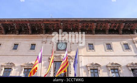 PALMA, SPANIEN - 26. APRIL 2023: Ein Tiefwinkelfoto einer Uhr und Fahnen auf einem historischen Gebäude in der Hauptstadt mallorcas Stockfoto