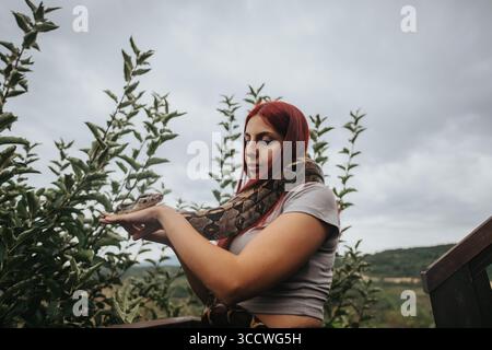 Mädchen mit rotem Haar hält eine große Schlange draußen Stockfoto