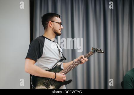 Junger Mann, der elektrische Gitarre in einer ungezwungenen Innenumgebung spielt Stockfoto