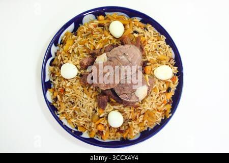 Traditionelles usbekisches Plov (Pilaw) serviert auf einer blauen Keramikplatte. Das Gericht besteht aus duftendem Reis, zartem Lamm oder Rindfleisch, gelben Karotten, Kichererbsen und Stockfoto
