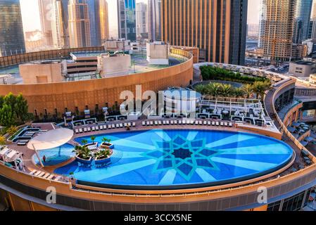 Dubai, VAE - 08. Januar 2012: Infinity-Pool auf dem Dach eines Hotels in Dubai Marina, eingerahmt von Liegestühlen, mit moderner Skyline von Wolkenkratzern Stockfoto