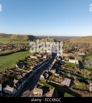 Die Ruinen von Corfe Castle aus der Vogelperspektive stehen stoisch inmitten eines Wandteppichs aus grünen Hügeln und malerischen Dorfhäusern, die lange Schatten in das sanfte Licht werfen, Corfe Castle, England. Stockfoto