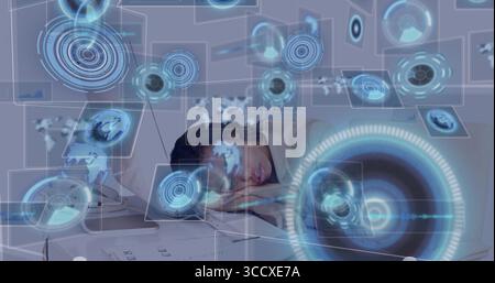 Frau in Hoodie und Brille, die am Arbeitsplatz schläft, mit offenen Laptoppapieren holographische Diagramme Stockfoto