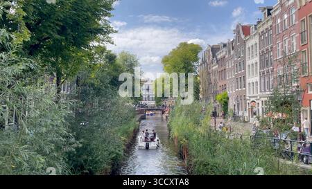 Amsterdam Niederlande 10. August 2025 Ein Boot fährt entlang der schmalen Leliegracht. Die Wände des Kanals wurden durch einen Koffer-Damm verstärkt, der Bereich dazwischen mit Weiden und anderen Bäumen bepflanzt wurde. Achterstallig, onderhoud, Kassettendamm, Reparaturen, wallen Stockfoto
