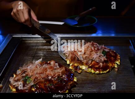 Der Koch kocht ein Okonomiyaki auf dem Eisenteller, ein beliebtes lokales Essen in Japan Stockfoto