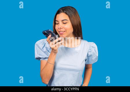 Lächelnde Geschäftsfrau mit Smartphone, die Audionachrichten auf blauem Hintergrund aufnimmt Stockfoto