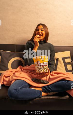 Glückliche Frau, die sich auf dem Sofa entspannt, Popcorn isst und einen Film ansieht Stockfoto