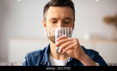 Nahaufnahme eines Mannes mittleren Alters, der zu Hause Wasser trinkt Stockfoto