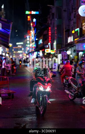 Eine lebhafte Nachtszene in Bui Vien, Ho Chi Minh City, aufgenommen im September 2024, mit Rollerfahrern auf nassen Straßen, die von Farbfu beleuchtet werden Stockfoto