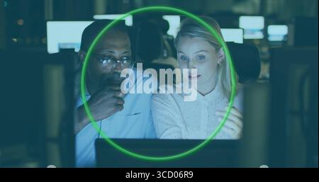 Zwei Fachleute diskutieren Daten und Gesten, die an schwach beleuchteten Bürotischen arbeiten und auf leuchtenden Monitoren arbeiten Stockfoto