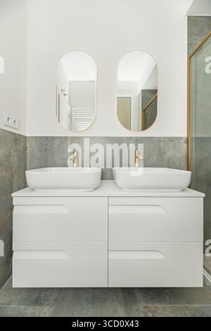 Minimalistisches Badezimmer mit quadratischem Porzellanwaschbecken, Armaturen im deutschen Stil und einer rahmenlosen Duschkabine Stockfoto