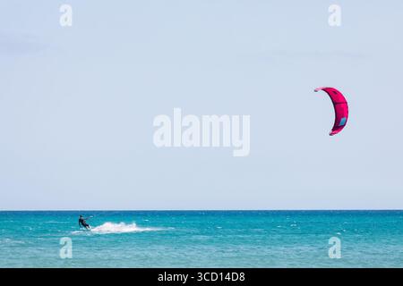 Kiteboarder surfen und den Wind und den Sommer im Meer genießen. Buntes Segeln in der Luft mit der glänzenden Oberfläche des sonnendurchfluteten Ozeans Stockfoto