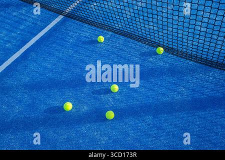 Gelbe Padelbällchen auf einem blauen Hof neben dem Netz verstreut. Stockfoto