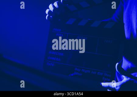 Ein Crew-Mitglied bereitet sich darauf vor, den Beginn einer neuen Aufnahme mit einer Tafel in einem schwach beleuchteten Filmstudio zu markieren, während die Atmosphäre mit Antizip aufgeladen ist Stockfoto