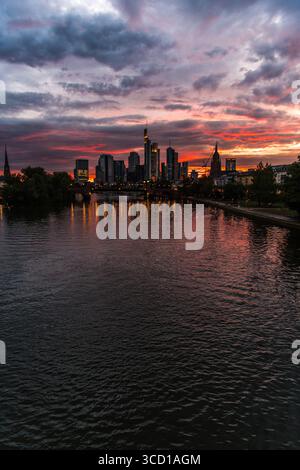 Leuchtende Wolken erfüllen den Himmel, während die Sonne hinter Frankfurts Skyline untergeht, reflektieren den Fluss darunter und schaffen eine atemberaubende Abendatmosphäre Stockfoto