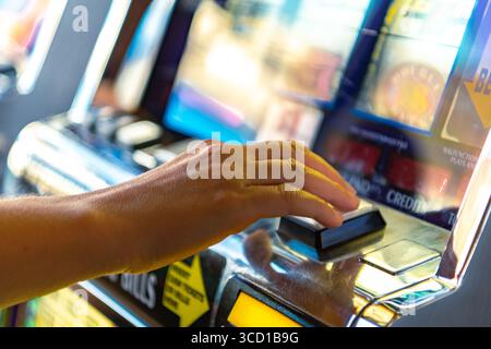 Eine Person drückt eifrig den Knopf an einem Spielautomaten in einem lebhaften Casino, umgeben von bunten Lichtern und Geräuschen, was eine aufregende Atmosphäre schafft. Stockfoto