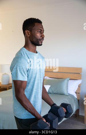 Afroamerikaner trainiert im Schlafzimmer, trägt T-Shirt mit schwarzen Hexen-Kurzhanteln, Kopierraum Stockfoto