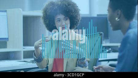 Eine Frau mit lockigen Haaren, die einen Blazer trägt, erklärt die Datenüberlagerung im Büro, mit Monitoren Stockfoto