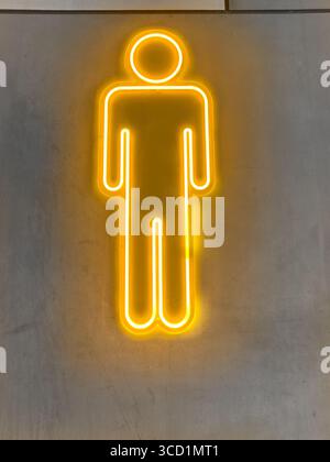 Helles gelbes Neonlicht in Form einer einfachen männlichen menschlichen Figur auf einem grauen Betonwandhintergrund - Restaurantschild für männliche Toiletten der Herren Stockfoto