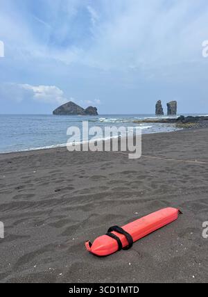 Orange Rettungsgürtelboje am schwarzen Sand von Mosteiros Beach auf den Azoren. Stockfoto