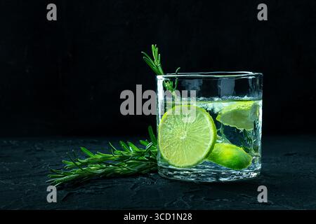 Gin Tonic, ein Glas Gin mit Limette, Rosmarin und viel Eis, Seitenansicht auf schwarzem Hintergrund, mit Kopierraum Stockfoto