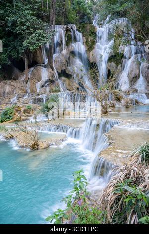 Atemberaubender vertikaler Blick auf die Kuang Si Wasserfälle, die in türkisfarbene Pools inmitten des üppigen Waldes in Luang Prabang, Laos, fließen Stockfoto