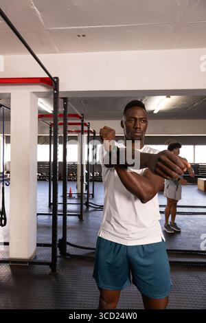 Verschiedene Männer, die sich im Fitnessstudio auf das Training vorbereiten, mit einem Metallaufsatz, Kampfseilen und Wasserkettlebells Stockfoto
