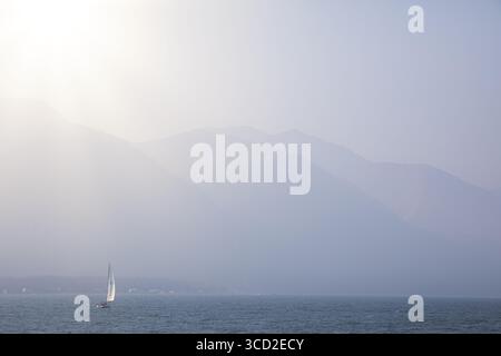 Blick auf ein einsames Segelboot, das über die ruhigen Gewässer der Resurrection Bay gleitet, mit den trüben Bergen des Kenai Fjords National Park im di Stockfoto