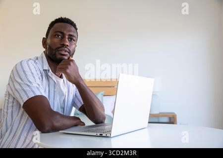 Mittelgroßer afroamerikanischer Mann, der an silbernem Laptop im Schlafzimmer, im Kopierraum arbeitet Stockfoto