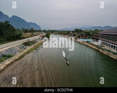 Blick auf Longtail-Boote auf dem Fluss Nam Song mit Riverside Resorts und Karstbergen in Vang Vieng, Laos Stockfoto