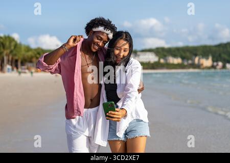 Vielfältige Paare verbunden, mit Technologie und sozialen Medien, während Sie Momente am Strand genießen Stockfoto